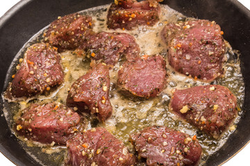 Smażenie mięsnych kąsków na oleju. Mięso w przyprawach na patelni. Smażenie polędwiczek wieprzowych.