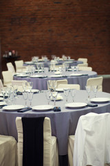 Preparation for a banquet. The tables are covered with lilac tablecloth. Wine glasses are on the tables in the restaurant.