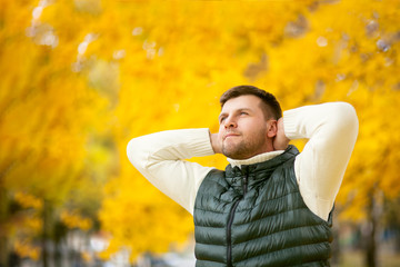 portrait of a handsome man with hands behind his head in an autumn park