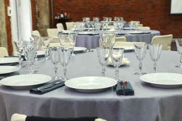 Preparation for a wedding banquet. The tables are covered with lilac tablecloth. Wine glasses are on the tables in the restaurant.