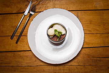 ice cream sweet dessert on a white plate on a wooden table in an Italian retor. Ingredients white ice cream with mint and cocoa in a transparent tequal glass with smoke.