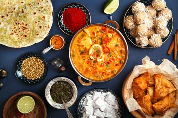 Indian cuisine on diwali holiday: tikka masala, samosa, patties and sweets with mint chutney and spices. Dark blue background