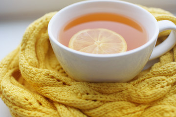 Mug of hot tea in a scarf on a window sill at a window