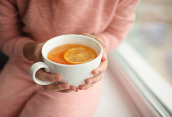 Cup of hot tea in hands at a window. Close up