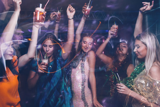 New Year dance party in night club. Happy friends company with drinks, Christmas celebration in motion. Disco people in blurred colors, modern youth life
