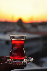 traditional cup with Turkish black tea in hand against the backdrop of the setting sun.
