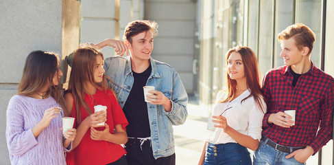 Students enjoying cup of coffee to go on street. Young people communicating outdoor at morning with cup of energy drink