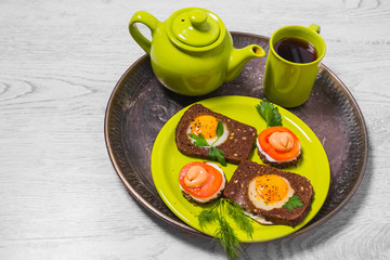 Breakfast - toast with processed cheese tomato, fried eggs , fried eggs, teapot cup of tea on a gray background.