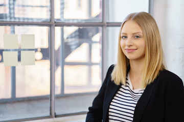 junge frau steht lächend am fenster im büro