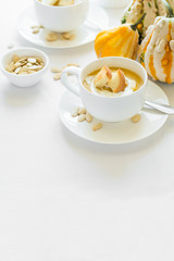 Two cups with fresh pumpkin cream soup decorated cream, seeds and crackers on white table cloth