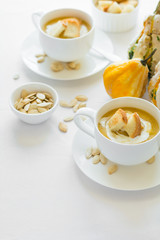 Two cups with fresh pumpkin cream soup decorated cream, seeds and crackers on white table cloth