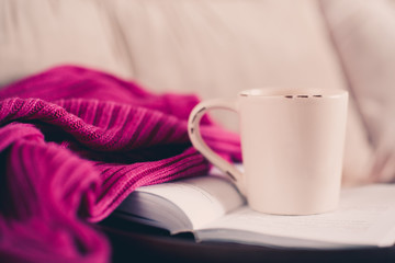Cup of tea staying on open book with knitted sweater in bed. Good morning.
