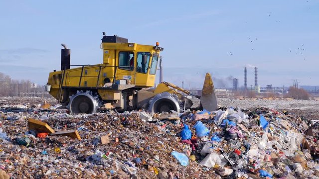 A landfill truck levels out the first garbage layer at a junkyard.