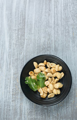 Roasted peanuts with chili pepper and coriander served in a small black dish. Rustic wooden background. Copy space. 