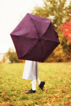 Happy funny child with umbrella. Girl is wearing funny hat and enjoying autumn and life. Kid playing on the nature outdoors.