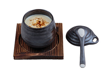 Isolated Japanese custard pudding torched caramel on top served in black ceramic cup on wooden plate with lid and spoon.