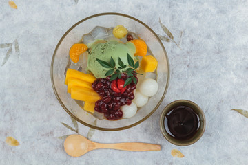 Top view of Matcha (Green Tea) ice cream served with jack fruit, lychee, orange, coconut jelly and red bean paste served with maple syrup and wooden spoon on washi (Japanse paper).