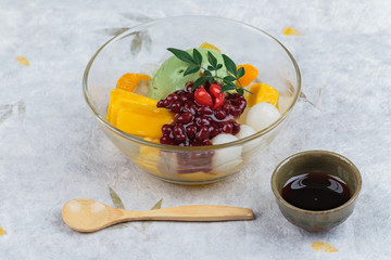 Matcha (Green Tea) ice cream served with jack fruit, lychee, orange, coconut jelly and red bean paste served with maple syrup and wooden spoon on washi (Japanse paper).