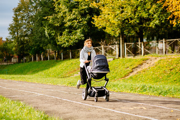 Young mother jogging with a baby buggy at stadium track in fall autumn time. Motherhood, sport, run, fitness multitacking concept.