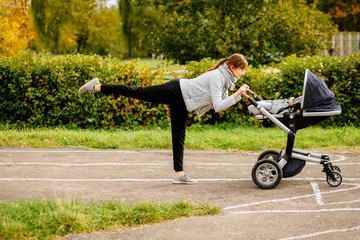 Side view of young smiling sporty woman with baby stroller in warm clothes warming up - doing...