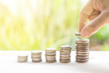 Closeup of hand put coins to stack of money with nature background-Business growing and saving...