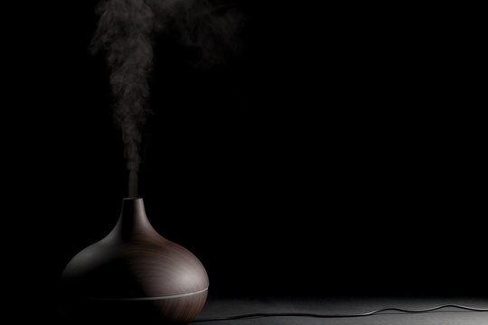 Electric aromatherapy device. Electronic diffuser gadget in use against black background.