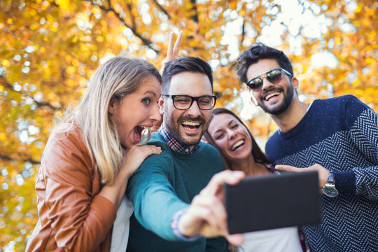 Group of four funny friends taking selfie with a smart phone in park
