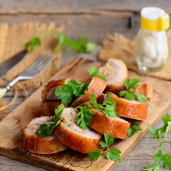 Baked stuffed chicken rolls on a wooden board. Fork, knife, salt shaker, parsley on a wooden table. Rustic style. Chicken rolls lunch meat