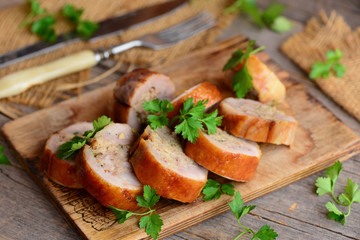 Roasted stuffed chicken rolls on a wooden board. Fork, knife on a wooden table. Rustic style. Chicken roll lunch meat recipe