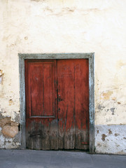 old wooden decaying closed double door with peeling green paint on the frame set in a crumbling white cement wall