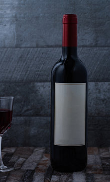 Botella de vino tinto sobre piedra y fondo ceramica gris y mitad de copa en fotograma