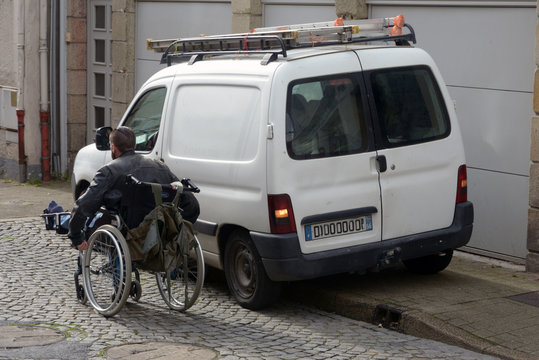 Personne en fauteuil roulant obligée de passer sur la route à cause d'une voiture mal garée 