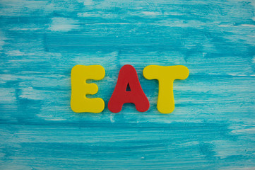 Eat in colorful letters on blue wood background