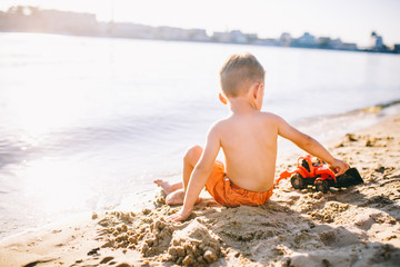 child boy playing on the beach near the river toy red tractor