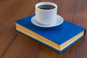 Cup of coffee and book on wooden table