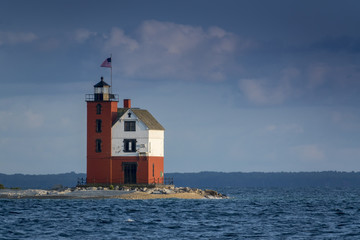 Fototapeta na wymiar Beautifully restored Historic Round Island Lighthouse on Mackinac Island Michigan. Its bright colors stand out dramatically surrounded by the blue waters and pine tree forest of Lake Huron.