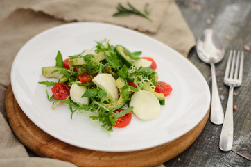 Salad of mozzarella, avocado, cherry tomatoes and arugula in a plate