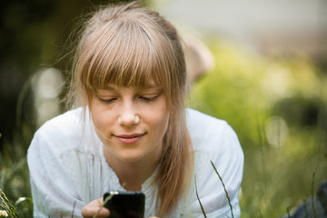 Young woman with fringe lying down on her stomach on grass with mobile phone