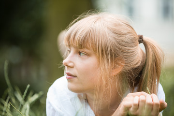 Portrait of an attractive young woman with fringe lying down on her stomach on grass