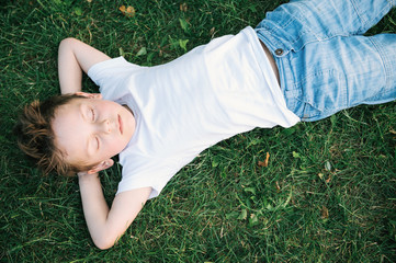 handsome little boy lying on the green grass relaxing