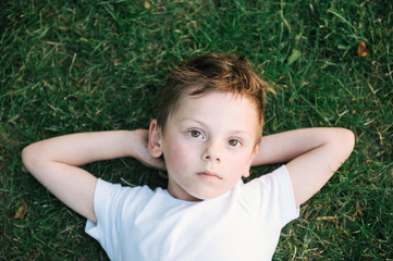 beautiful pensive kid lying on green grass