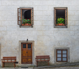 Fototapeta na wymiar Wooden door on empty concrete gray blocks wall with upper two windows opening decorated with flower