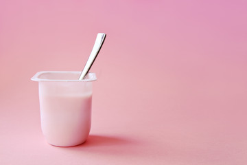 Delicious strawberry yogurt or pudding  in white plastic cup on pink background with copy space. Strawberry pink yoghurt with spoon in it. Minimal style.