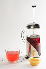 Hot drink of cranberries and raspberries in а teapot and in a cup with honey on white background