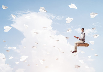 Handsome man student reading book and paper planes flying around