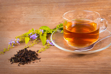 Cup of green tea and spoon of dried green tea leaves on wooden background
