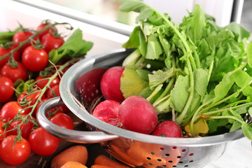 Colander with fresh radish and vegetables on windowsill