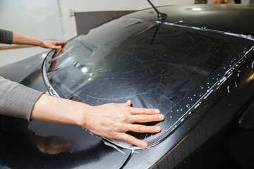 Master installs a tint film for the car glass with a hairdryer and spatula with glare of light....