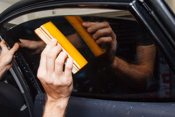 Master installs a tint film for the car glass with a hairdryer and spatula with glare of light....