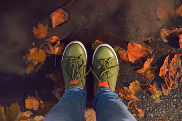 Selfie legs close-up in blue jeans and green sneakers standing in a puddle with yellow leaves in autumn in the park